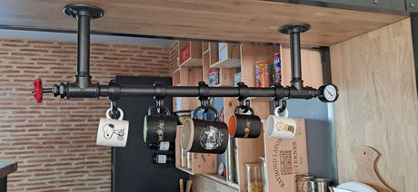 Porte-tasses industriel en tubes 3/4″ fixé sous une tablette en bois, avec cinq tasses suspendues à des crochets