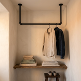 Aan het plafond hangend kledingrek van zwarte buis in een kleedhoek, boven een houten plank